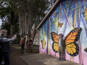 FILE - Leslee Russell of Livermore, Calif. takes a picture of her husband Dave Russell in front of a mural outside the Butterfly Grove Inn near the Monarch Grove Sanctuary in Pacific Grove, Calif., on Nov. 10, 2021. The number of Western monarch butterflies overwintering in California rebounded to more than 247,000 a year after fewer than 2,000 appeared, but the tally remained far below the millions that were seen in the 1980s, leaders of an annual count said Tuesday, Jan. 25, 2022.