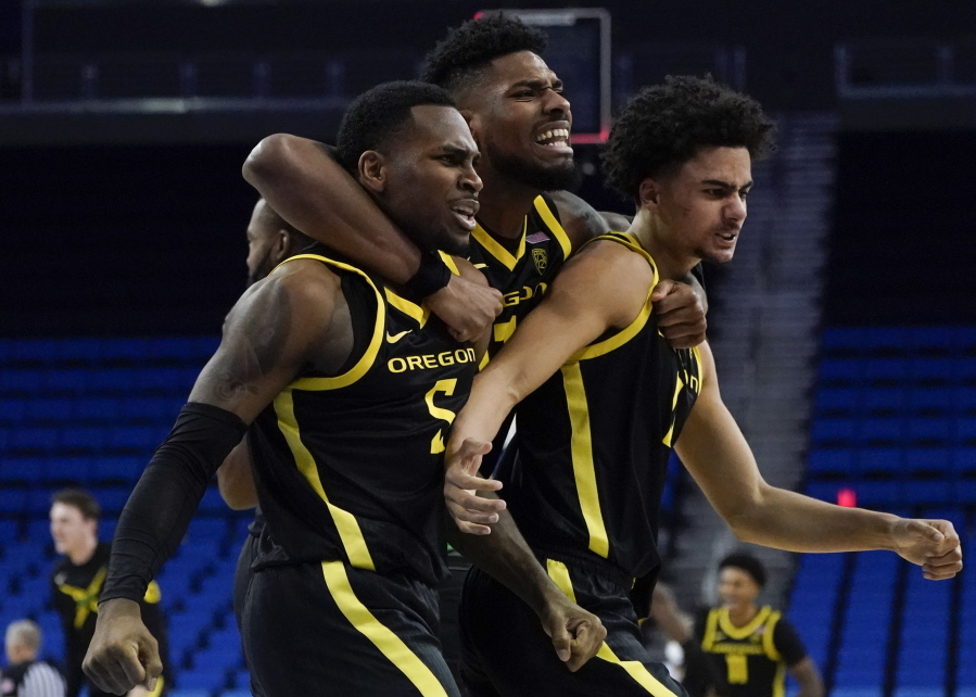 From left, Oregon guard De'Vion Harmon, forward Quincy Guerrier, and guard Will Richardson celebrate after winning 84-81 in overtime of an NCAA college basketball game against UCLA in Los Angeles, Thursday, Jan. 13, 2022.
