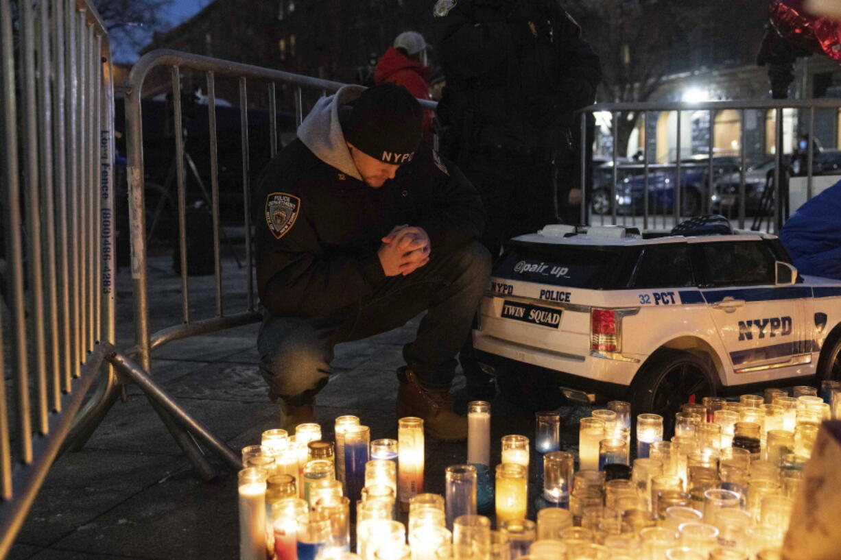 A police officer prays at a makeshift memorial outside the New York City Police Department's 32nd Precinct, near the scene of a shooting days earlier in the Harlem neighborhood of New York, Monday Jan. 24, 2022.