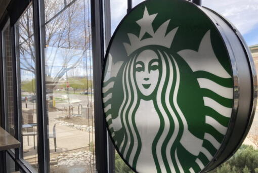 A sign bearing the corporate logo hangs in the window of a Starbucks open only to take-away customers in this photograph taken Monday, April 26, 2021, in southeast Denver.  Starbucks is no longer requiring its U.S. workers to be vaccinated against COVID-19, reversing a policy it announced earlier this month. The Seattle coffee giant says, Wednesday, Jan. 19, 2022,  it's responding to last week's ruling by the U.S. Supreme Court.