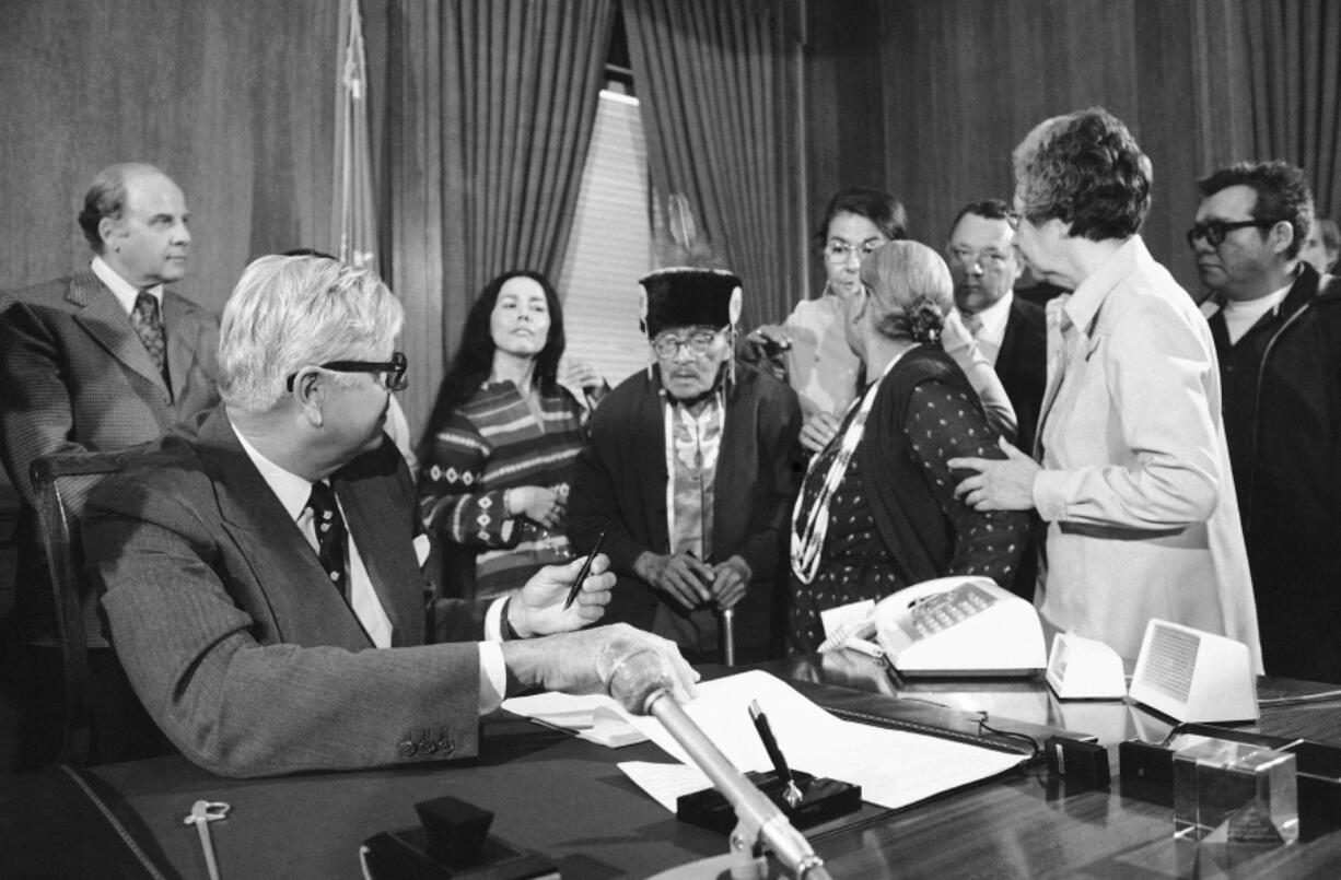 FILE - Interior Secretary Rogers Morton finishes signing a deed conveying the tribal land of the Menominee Indians of Wisconsin back to reservation status in a Washington ceremony, on April 22, 1975. The reservation status had been terminated in the early 1960s and the land converted into Wisconsin's 72nd county. From left are: Sen. Gaylord Nelson, D-Wis., Morton; Ada Deer, chairperson of the Menominee Restoration Committee; Ernest Neconish, 90, a tribal elder; an unidentified man; and Neconish's wife, Jane, 73. In 2022, Native American tribes are marking 50 years since the U.S. government's termination policy, considered an economic and human rights disaster, came to an end, making way for self-determination. More than 100 tribes were terminated under the policy, resulting in the loss of more than 1.3 million acres.