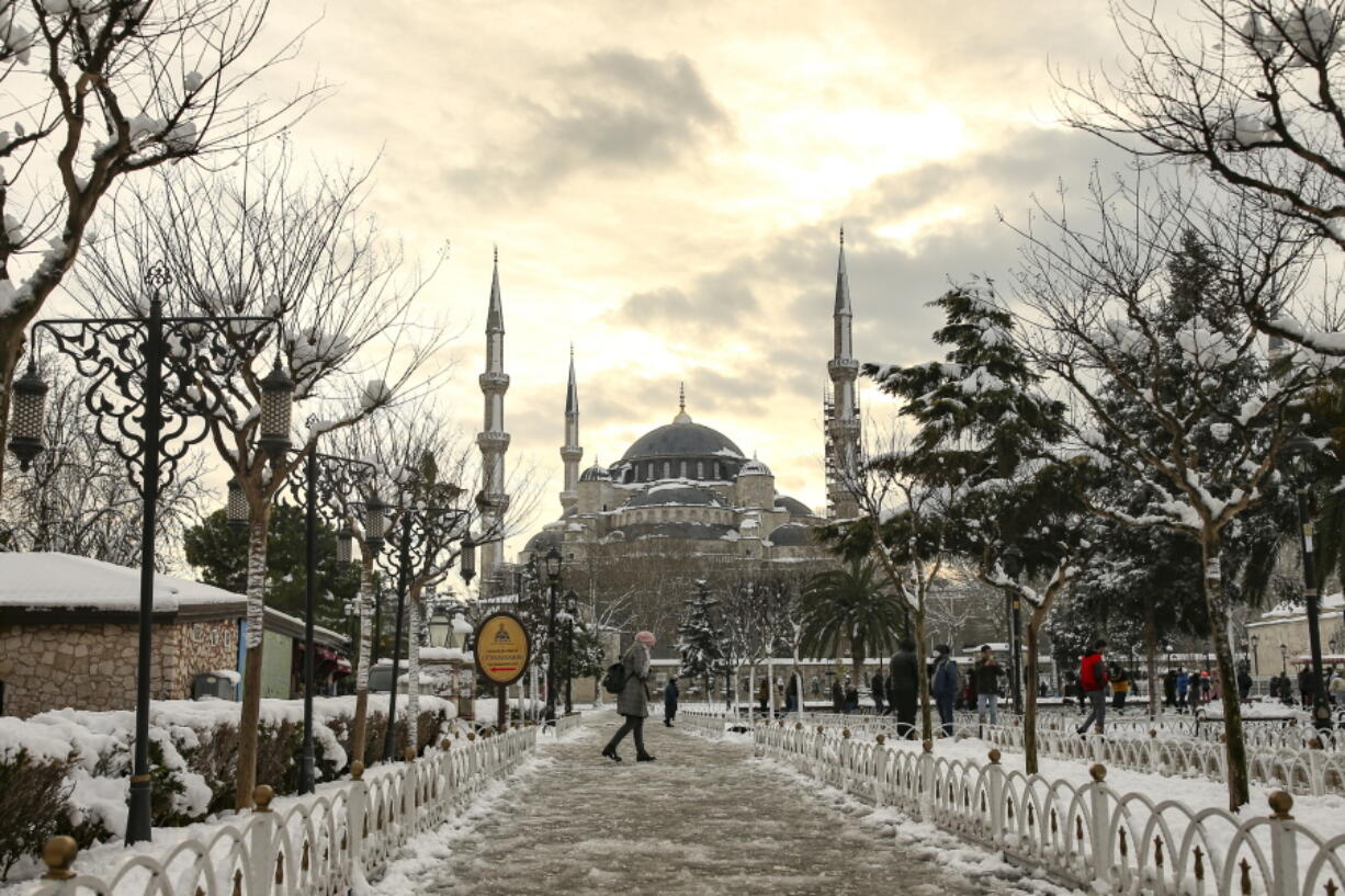 People walk in a snow-covered park with the iconic Haghia Sophia in the background at Istanbul, Tuesday, Jan. 25, 2022. Rescue crews in Istanbul and Athens on Tuesday cleared roads that had come to a standstill after a massive cold front and snowstorms hit much of Turkey and Greece, leaving countless people and vehicles in both cities stranded overnight in freezing conditions.