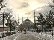 People walk in a snow-covered park with the iconic Haghia Sophia in the background at Istanbul, Tuesday, Jan. 25, 2022. Rescue crews in Istanbul and Athens on Tuesday cleared roads that had come to a standstill after a massive cold front and snowstorms hit much of Turkey and Greece, leaving countless people and vehicles in both cities stranded overnight in freezing conditions.
