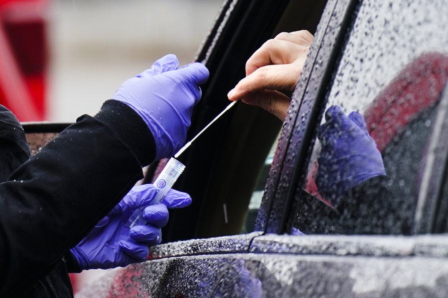 FILE - A driver places a swab into a vial at a free drive-thru COVID-19 testing site in the parking lot of the Mercy Fitzgerald Hospital in Darby, Pa., Thursday, Jan. 20, 2022. A requirement to get vaccinated against COVID-19 kicks in Thursday, Jan. 27,  for millions of health care workers in about half the states.