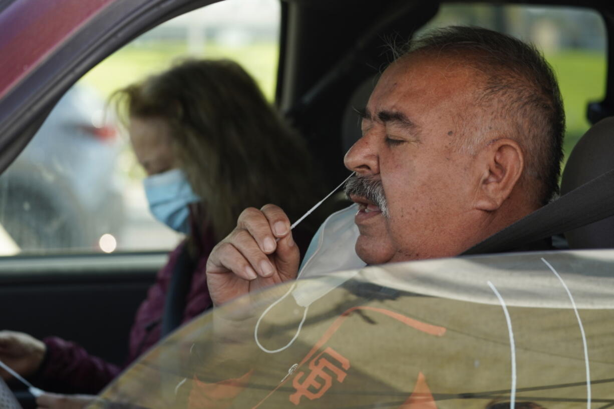 FILE - Jose Alfrtedo De la Cruz and his wife, Rogelia, self-test for COVID-19 at a No Cost COVID-19 Drive-Through event provided the GUARDaHEART Foundation for the City of Whittier community and the surrounding areas at the Guirado Park in Whittier, Calif., on Tuesday, Jan. 25, 2022.  Omicron, the highly contagious coronavirus variant sweeping across the country, is driving the daily American death toll higher than during last fall's delta wave, with deaths likely to keep rising for days or even weeks.