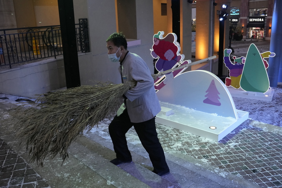 A sweeper wearing a mask to protect from the coronavirus walks past displays promoting winter sports in Beijing, China, Thursday, Jan. 20, 2022. The sweeping "zero-tolerance" policies that China has employed to protect its people and economy from COVID-19 may, paradoxically, make it harder for the country to exit the pandemic.