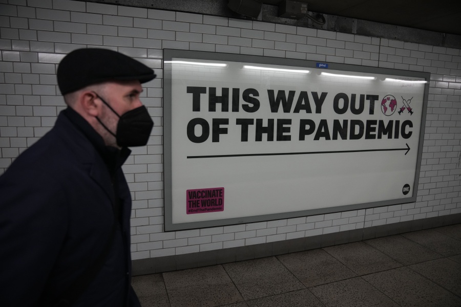 A man wearing a face mask to curb the spread of coronavirus walks past a health campaign poster from the One NGO, in an underpass leading to Westminster underground train station, in London, Thursday, Jan. 27, 2022. Most coronavirus restrictions including mandatory face masks were lifted in England on Thursday, after Britain's government said its vaccine booster rollout successfully reduced serious illness and COVID-19 hospitalizations. From Thursday, face coverings are no longer required by law anywhere in England.