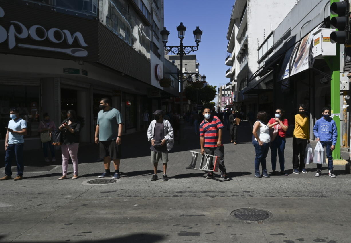 Wearing masks to curb the spread of the new coronavirus, people wait for a traffic light to change before crossing a street in San Jose, Costa Rica, Tuesday, Jan. 18, 2022.