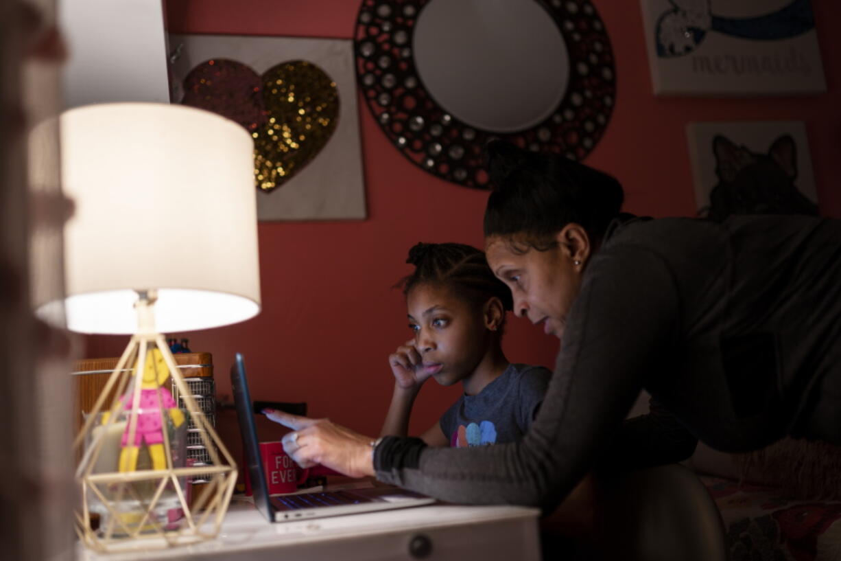 Abigail Schneider, 8, center, completes a level of her learning game with her mother April in her bedroom, Wednesday, Dec. 8, 2021, in the Brooklyn borough of New York. "I'm determined to push and push to get them the things that help them," said April Schneider.