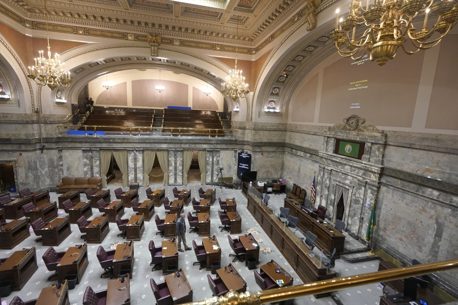 A lone worker walks on the floor of the Washington Senate, Thursday, Jan. 6, 2022, at the Capitol in Olympia, Wash. as the room was being prepared for the start of the 2022 legislative session, which opens Monday, Jan. 10, 2022. The new session will look much like the one a year ago: a limited number of lawmakers on site at the Capitol, and committee hearings being fully remote due to the ongoing COVID-19 pandemic. (AP Photo/Ted S.