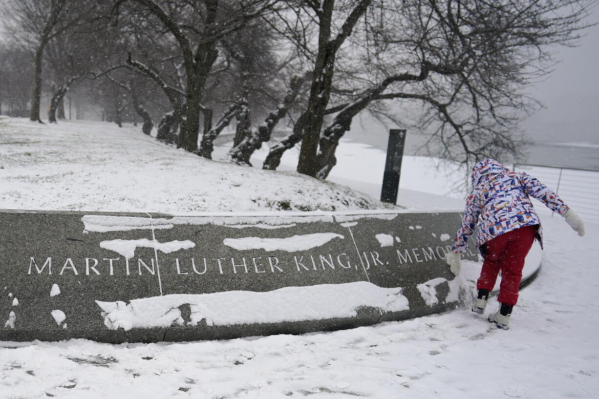 Shelby Batch, 12, of California, clears snow from the Martin Luther King, Jr. Memorial in Washington, Sunday, Jan. 16, 2022. Ceremonies scheduled for the site on Monday, to mark the Martin Luther King, Jr. national holiday, have been canceled because of the weather.