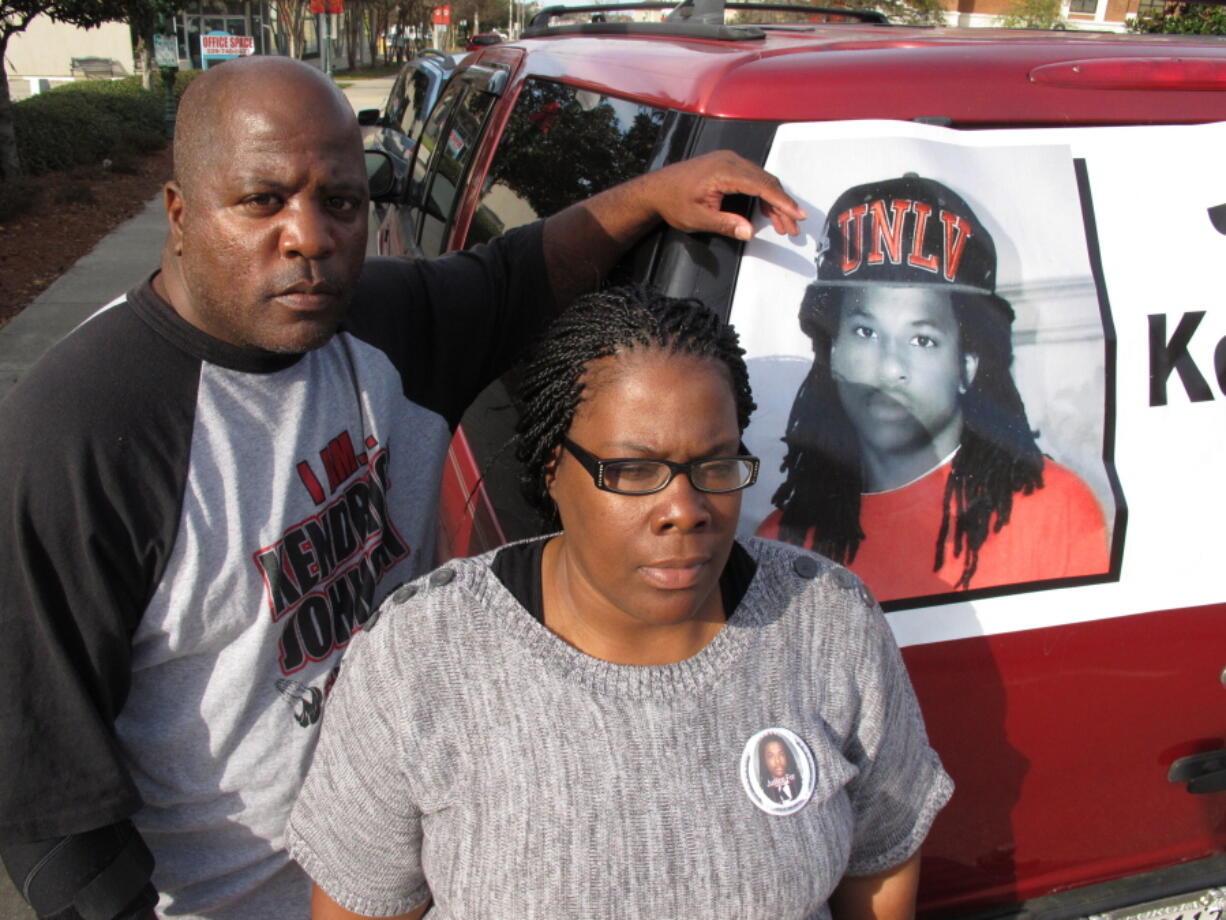 FILE - Kenneth and Jacquelyn Johnson stand next to a banner on their SUV showing their late son, Kendrick Johnson, on Dec. 13, 2013, in Valdosta, Ga. A Georgia sheriff who last year reopened an investigation into the 2013 death of Kendrick Johnson, a teenager found inside a rolled up gym mat at school, concluded, Wednesday, Jan. 26, 2022, there was no evidence of foul play after reviewing voluminous evidence collected by federal investigators.