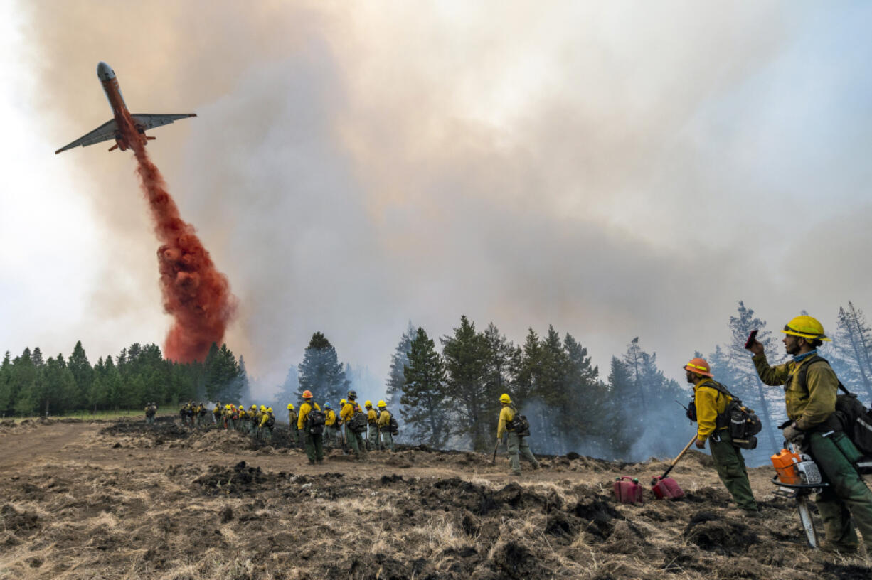 Wildland firefighters watch and take video with their cellphones as a plane drops fire retardant on Harlow Ridge above the Lick Creek Fire, southwest of Asotin, Wash., Monday, July 12, 2021. The fire, which started last Wednesday, has now burned over 50,000 acres of land between Asotin County and Garfield County in southeast Washington state.