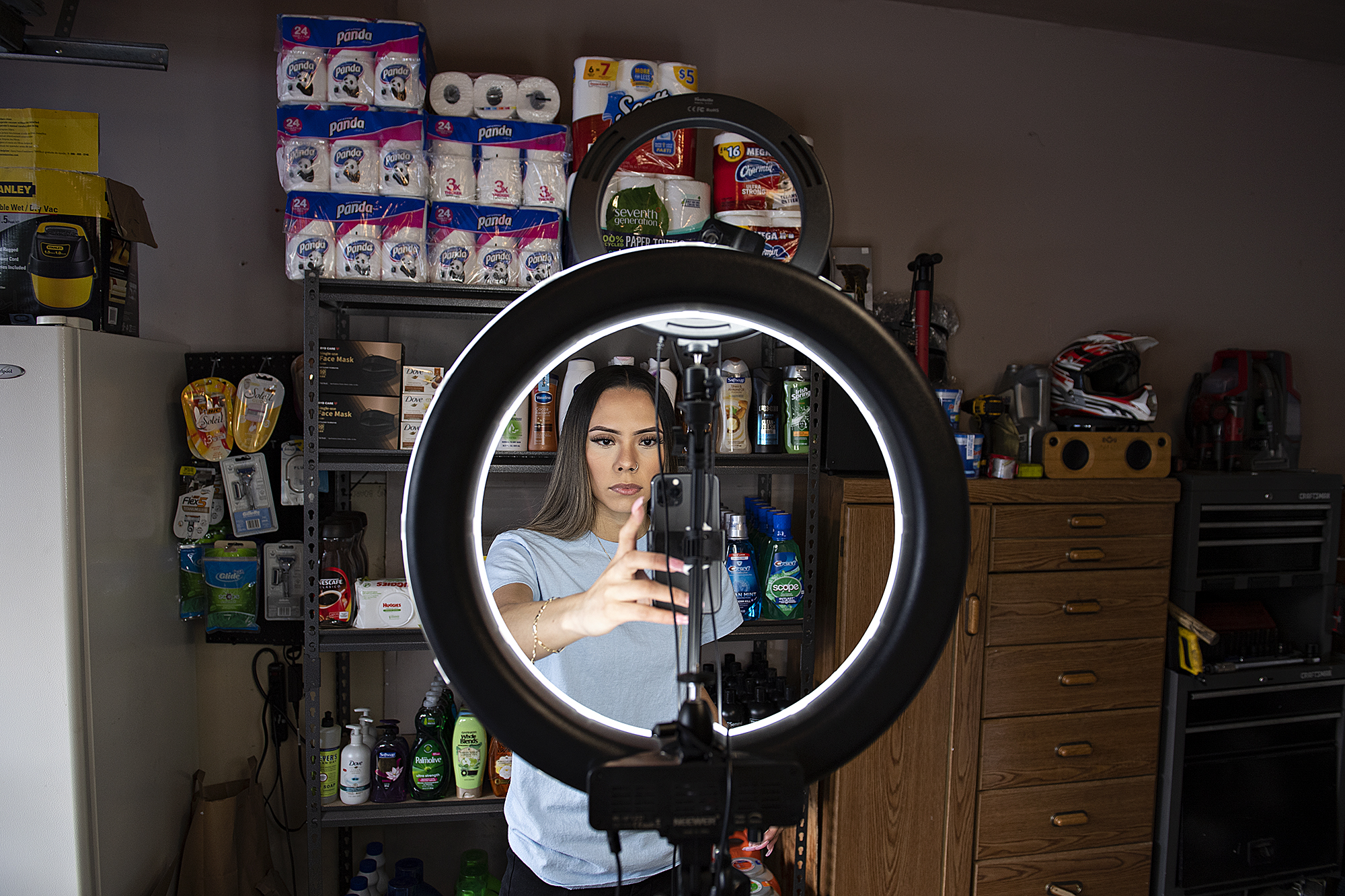 Social media influencer Jeimy Cruz, stands in front of a wall of products as she uses her smartphone to film a post for TikTok at her northeast Vancouver garage.