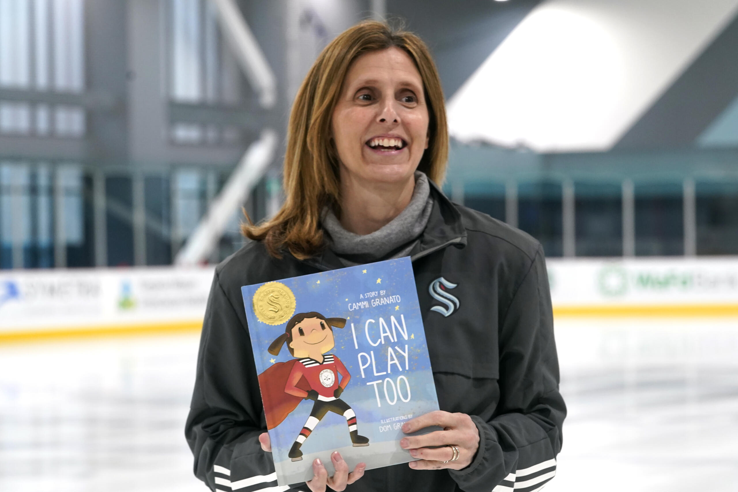 Seattle Kraken NHL hockey team pro scout Cammi Granato poses with her new book, "I Can Play Too," Wednesday, Feb. 2, 2022, in Seattle. For years, Hockey Hall of Famer Granato was asked to write a book about her experience in becoming one of the finest women's hockey players of all time. She finally has, but on her own terms and with a specific audience in mind—kids. And while her book is based around hockey and her personal experiences, Granato is hoping the message can resonate beyond the ice.
