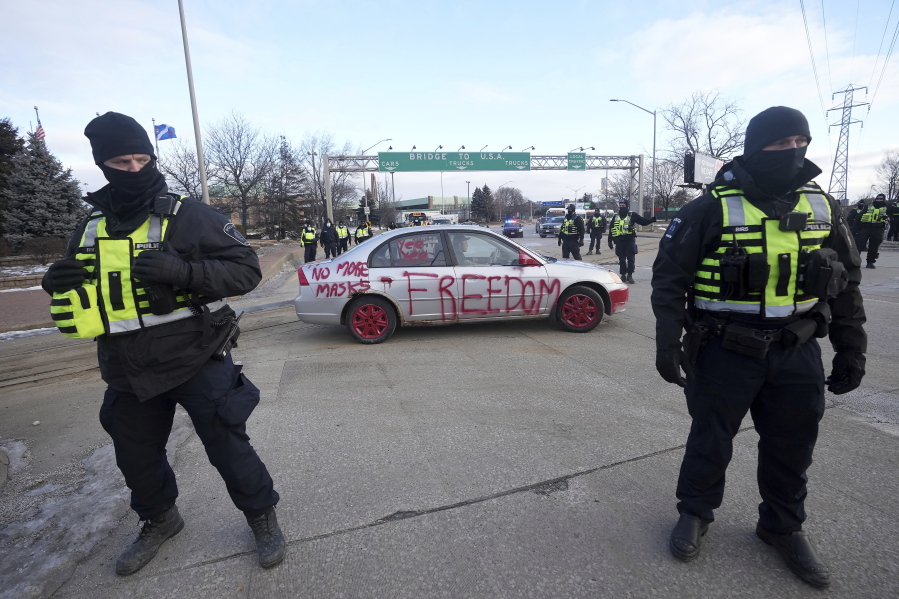 Police look on as a protest vehicle leaves a demonstration which has blocked traffic across the Ambassador Bridge by protesters against COVID-19 restrictions in Windsor, Ont., Saturday, Feb. 12, 2022. Canadian police have moved in to remove protesters who have disrupted Canada-US trade at the major bridge border crossing.