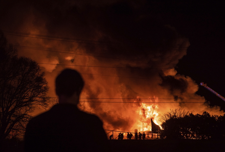 A bystander watches as Winston-Salem firefighters battle a structure fire at Weaver Fertilizer Co. on Monday, Jan. 31, 2022, in Winston-Salem, N.C.