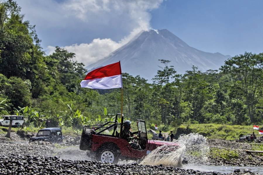 FILE - An Indonesian national Red-White flag waves from a car driven through an off-road track as Mount Merapi, one of the most active volcanoes in the country, is seen spewing volcanic smoke, during an Independence Day celebration in Sleman, Indonesia, Tuesday, Aug. 17, 2021. Dutch troops used "extreme violence" -- often deliberately -- during Indonesia's war for independence and military leaders and politicians in the Netherlands largely ignored the excesses, a long-running research project concluded in findings published Thursday, Feb. 17, 2022. In 2020, Dutch King Willem-Alexander formally apologized for his country's aggression while on a state visit to Indonesia.