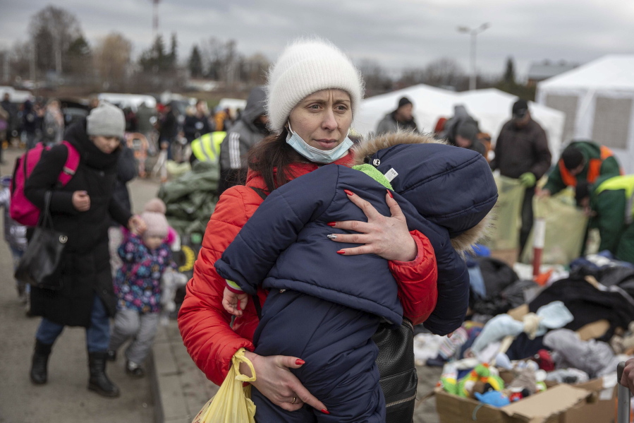 A woman carries her child as she arrives at the Medyka border crossing after fleeing from the Ukraine, in Poland, Monday, Feb. 28, 2022. The head of the United Nations refugee agency says more than a half a million people had fled Ukraine since Russia's invasion on Thursday.