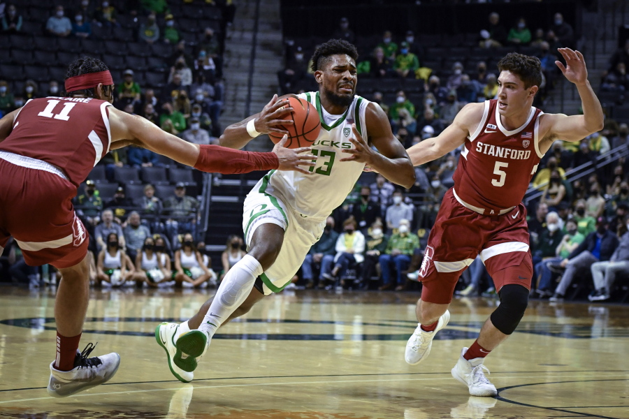 Oregon forward Quincy Guerrier (13) drives to the basket while guarded by Stanford forward Jaiden Delaire (11) and guard Michael O'Connell (5) during the first half of an NCAA college basketball game Thursday, Feb. 10, 2022, in Eugene, Ore.