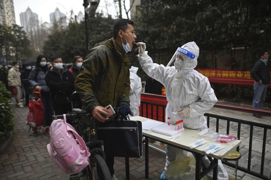 A man holding his bicycle with a school bag on it gets a throat swab during a mass COVID-19 test at a residential compound in Wuhan in central China's Hubei province, Tuesday, Feb. 22, 2022. Wuhan, the first major outbreak of the coronavirus pandemic has reported more than dozen new coronavirus cases this week, prompting the authority to step up precautious measures.
