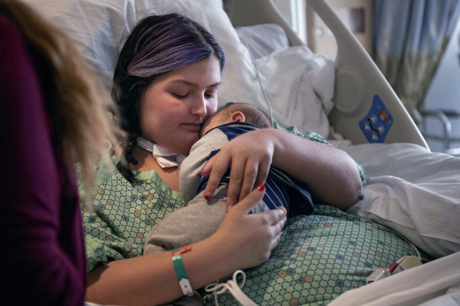 In this image provided by Kata Sasvari, Macenzee Keller, 20, of Manchester, N.H., clutches her two-month-old son Zachery for the first time since she giving birth, at the Dartmouth-Hitchcock Medical Center in Lebanon, N.H., Feb. 3, 2022. Keller delivered Zachery on Nov. 28, 2021, while on a ventilator at Catholic Medical Center in Manchester. N.H., after being stricken with COVID-19.