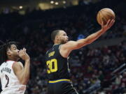 Golden State Warriors guard Stephen Curry, right, shoots in front of Portland Trail Blazers forward Trendon Watford during the first half of an NBA basketball game in Portland, Ore., Thursday, Feb. 24, 2022.