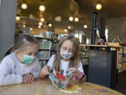 Leah Mulyar, 5, of Vancouver, left, and her sister, Isabel, 7, wear masks while enjoying a book at Vancouver Community Library on March 11, the final day of required indoor masking in Washington.