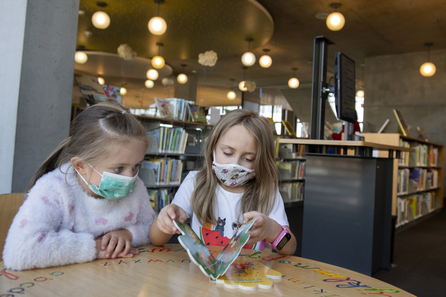 Leah Mulyar, 5, of Vancouver, left, and her sister, Isabel, 7, wear masks while enjoying a book at Vancouver Community Library on March 11, the final day of required indoor masking in Washington.