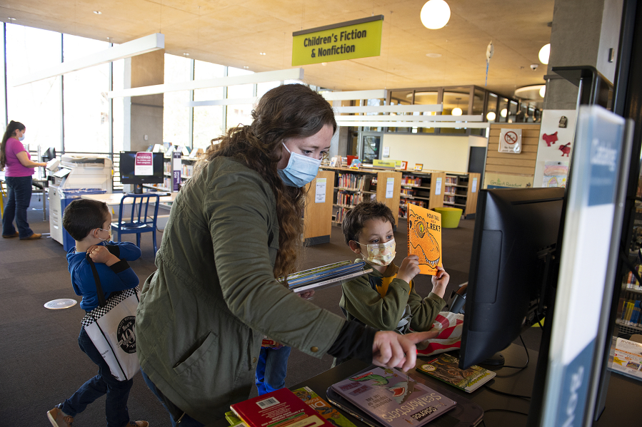 Visitors Ezekiel Clore, 5, from left, joins his mom, Kendra, and his brother, Jeremiah, 6, as they check out books while wearing masks at Vancouver Community Library on a Friday afternoon.