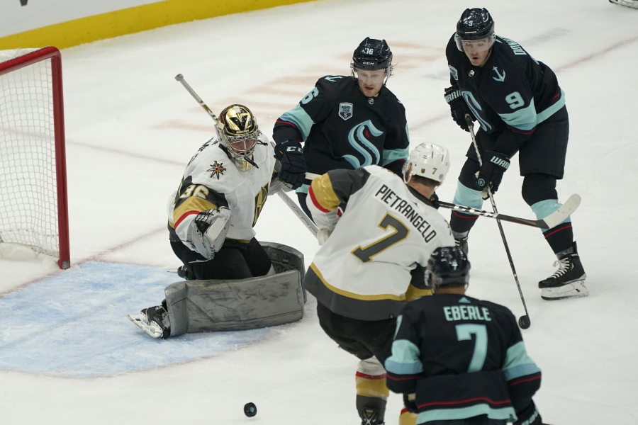 Vegas Golden Knights goaltender Logan Thompson deflects a shot as Seattle Kraken left wing Jared McCann, upper-center, and center Ryan Donato (9) look on during the second period of an NHL hockey game, Wednesday, March 30, 2022, in Seattle. (AP Photo/Ted S.