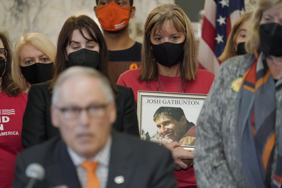 Kim Gatbunton, center, holds a photo of her son Josh Gatbunton, who was shot and killed during a 2008 robbery at an apartment in Tacoma, Wash., as she listens to Washington Gov. Jay Inslee, lower left, speak Wednesday, March 23, 2022, before signing a package of bills to tighten gun laws in Washington state at the Capitol in Olympia, Wash. (AP Photo/Ted S.