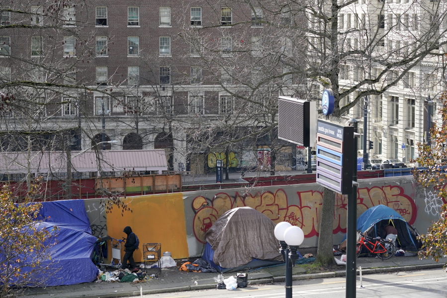 A person at left walks toward the entrance of a tent used by people experiencing homelessness, Tuesday, March 1, 2022, in downtown Seattle across the street from City Hall.  (AP Photo/Ted S.