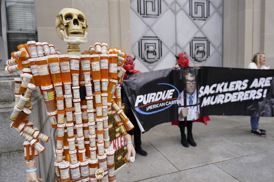 FILE - Pill Mann" made by Frank Huntley of Worcester, Mass., from his opioid prescription pill bottles, is displayed during a protest by advocates for opioid victims outside the Department of Justice, on Dec. 3, 2021, in Washington. Many families left heartbroken by opioid overdoses and addictions have been waiting for years to be able to tell another family - the Sacklers - about the damage their company, Purdue Pharma, did. Their chance arrives Thursday, March 10, 2022, in a federal court hearing to be conducted by video, during what could be the end of a long legal odyssey that will allow Purdue and the Sacklers to settle thousands of lawsuits.