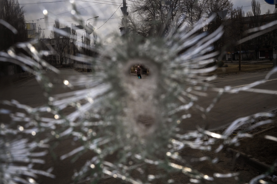 A man is seen through a bullet hole of a machine-gunned bus after an ambush in the city of Kyiv, Ukraine, Friday, March 4, 2022. While a small group of reservists were burying their comrade, 54-year-old Volodymyr Nezhenets, who was one of three killed on Feb. 26 in an ambush Ukrainian authorities say was caused by Russian 'saboteurs', a few kilometers away from the cemetery, the remains of the convoy Volodymyr was killed in 6 days ago still stands in the road with charred vehicles, a bus riddled with bullets, a spatter of blood on the drivers seat.