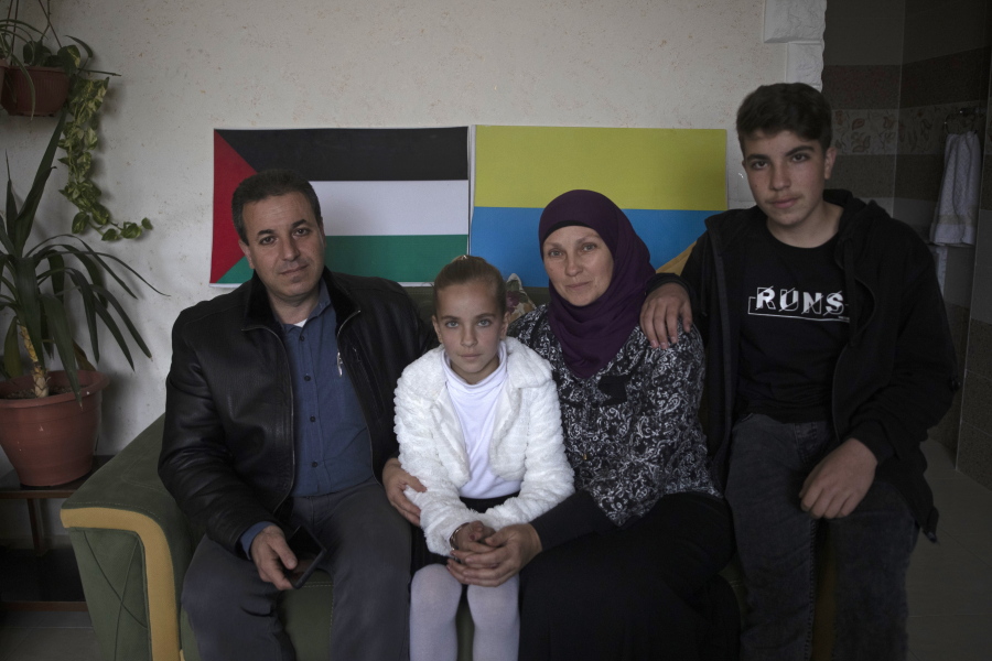 Ukrainian Oksana al-Astal sits with her Palestinian husband and their children as they pose for a photo in front of representations of Palestinian and Ukrainian flags decorating the living room of their home in Khan Younis, southern Gaza Strip, Sunday, March 13, 2022. The al-Astal family is among dozens of Palestinian-Ukrainian families in the isolated territory who have experienced several wars firsthand -- the most recent last May -- and are now watching another unfold in Ukraine, where many of them have loved ones.