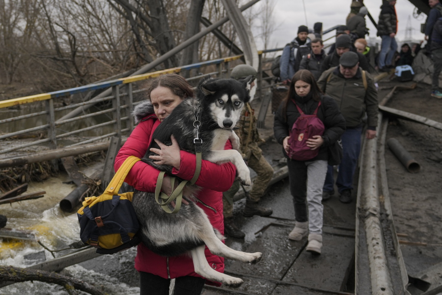 A woman holds a dog while crossing the Irpin River on an improvised path under a bridge as people flee the town of Irpin, Ukraine, on March 5.