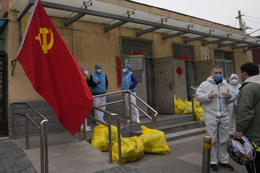 Community workers outside a locked down community chat near a Communist Party flag and trash bags labelled as hazardous waste on Thursday, March 17, 2022, in Beijing. Even as authorities lock down cities in China's worst outbreak in two years, they are looking for an exit ramp from what has been a successful but onerous COVID-19 prevention strategy.
