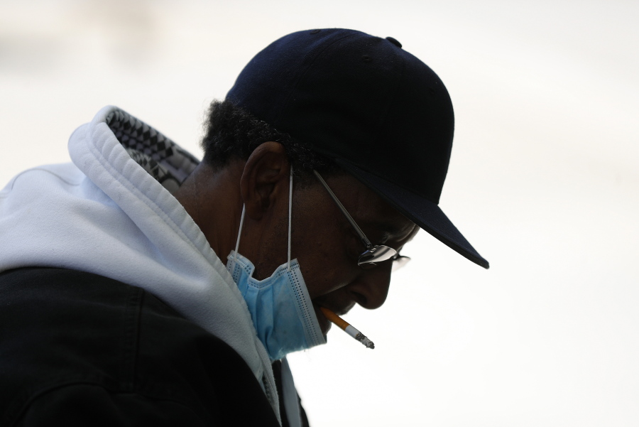 FILE - A man with a protective mask smokes a cigarette while waiting for a bus in Detroit, Wednesday, April 8, 2020. U.S. cigarette smoking dropped to a new all-time low in 2020, with 1 in 8 adults saying they were current smokers, according to survey data released Thursday, March 17, 2022, by the Centers for Disease Control and Prevention. Adult e-cigarette use also dropped, the CDC reported.