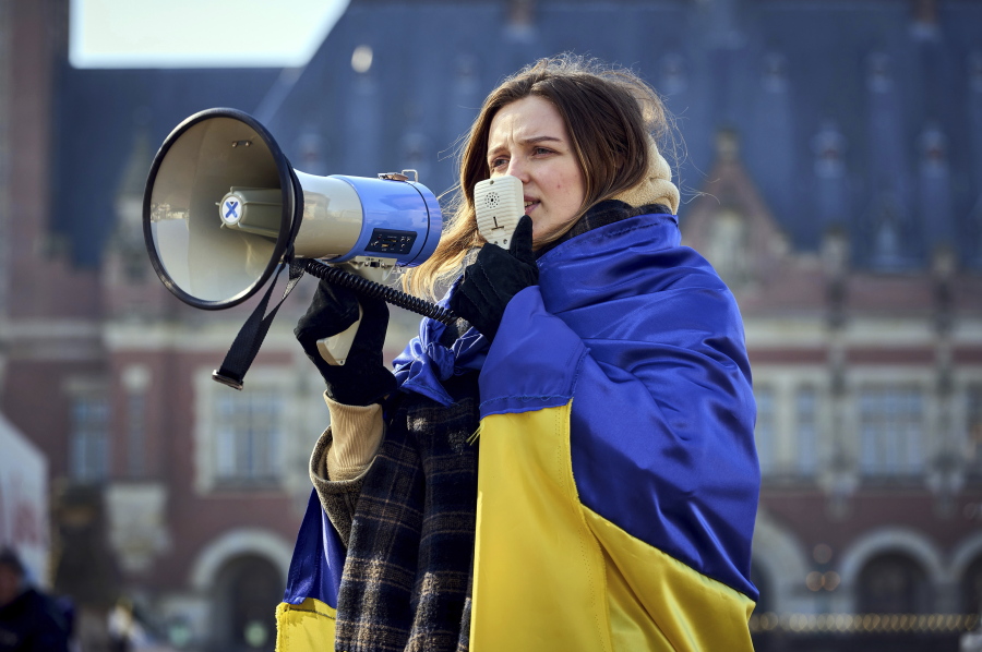 A woman is wrapped in the Ukrainian flag and shouts through a megaphone during a demonstration in front of the International Criminal Court in The Hague, Netherlands, Monday, March 7, 2022. A representative for Kyiv has urged the United Nations' top court to order Russia to halt its devastating invasion of Ukraine, at a hearing snubbed by Russia.