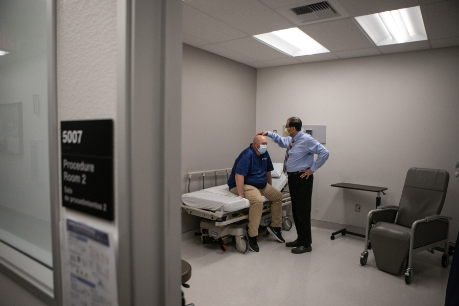 Rob Purdie, left, who has valley fever, checks in with his doctor at the same clinic where he serves as the Program Development Coordinator at the Valley Fever Institute at Kern Medical on March 22, 2022, in Bakersfield, California. Infectious Disease Physician Dr. Arash Heidari examines the port on Rob's head that is used to deliver medicine to treat his Valley Fever.