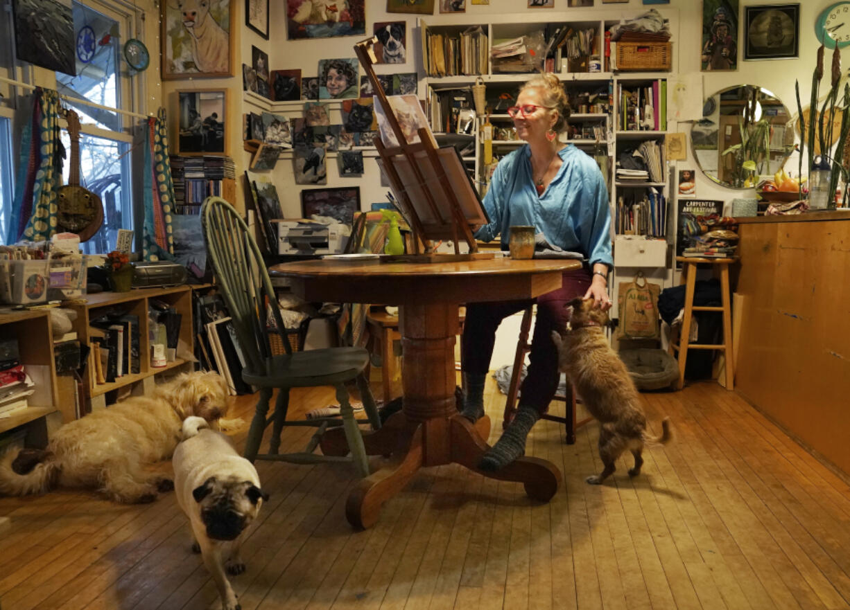 Artist Kat Corrigan works on one of her paintings for her 30 cats in 30 days project from her home, as family dogs rest and stir around her, Tuesday, March 15, 2022, in Minneapolis.