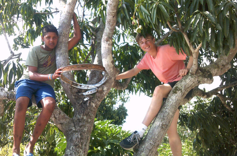 Columbia River High School sophomore Peter Lubisich, right, sits in a mango tree with a teenager from El Rodeo, Dominican Republic. Before Courts For Kids built an outdoor sports court, the town's youth played basketball on a makeshift hoop nailed to the tree.