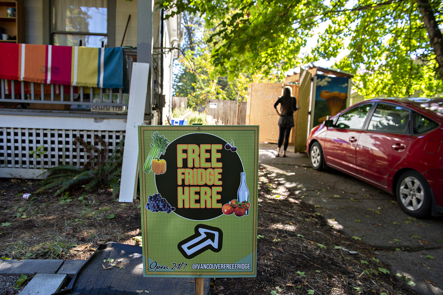 A sign greets visitors as Gretta Anderson looks over contents of the free food pantry and fridge at her Vancouver home Monday afternoon, Sept. 20, 2021. The Vancouver Free Fridge project is up to three fridges, but they're also being regulated by city codes over the structure, causing program leaders to start a petition.
