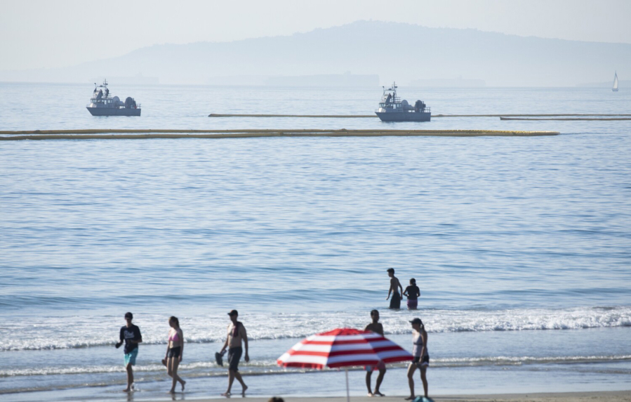 Beachgoers at Newport Beach enjoy the afternoon as boats drag oil booms offshore on Sunday, Oct. 3, 2021. (Myung J.