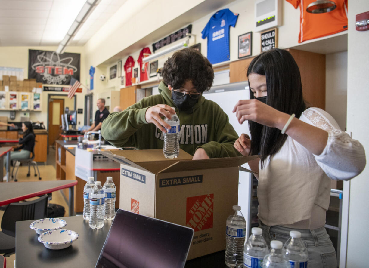 Union High School freshmen Victor Vitorino, left, and Savannah Lee pack a box full of water bottles and bowls Thursday at Union High School. The pair are two of hundreds of students participating in an after-school STEM Academy that leads simple experiments for young children in Evergreen Public Schools as a way to garner interest in science and math at a young age.