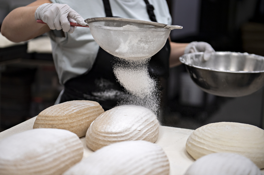 Olga Mikhalets, proprietor of Sweet Touch Bakery in Vancouver, sprinkles rice flour over shaped sourdough loaves. She started making her own dough for loaves sold in the store after supply chain disruptions.