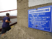 FILE - A man jogs past a sign about crisis counseling on the Golden Gate Bridge in San Francisco, Aug. 3, 2021.  People in crisis and those trying to help them will have a new three-digit number, 988, to reach the national suicide prevention network starting in July. Federal health officials on Monday are announcing more than $280 million to smooth the transition from the current 10-digit number.
