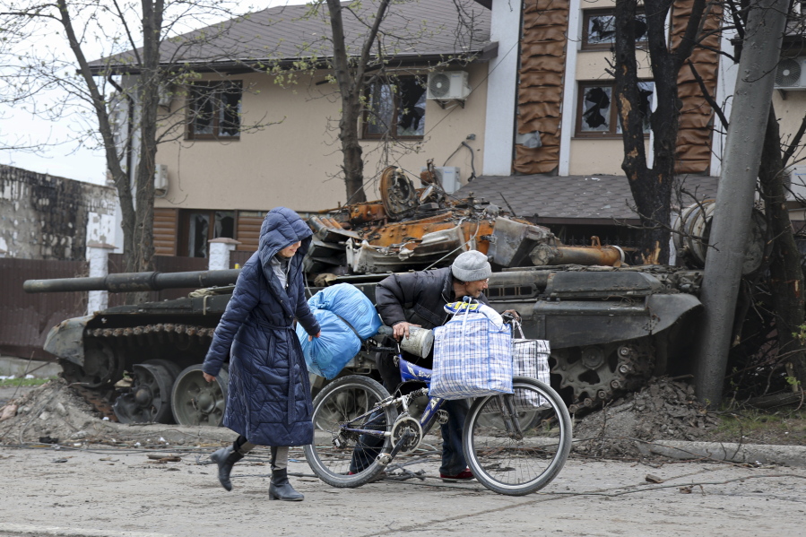 Local civilians walk past a tank destroyed during heavy fighting in an area controlled by Russian-backed separatist forces in Mariupol, Ukraine, Tuesday, April 19, 2022. Taking Mariupol would deprive Ukraine of a vital port and complete a land bridge between Russia and the Crimean Peninsula, seized from Ukraine from 2014.