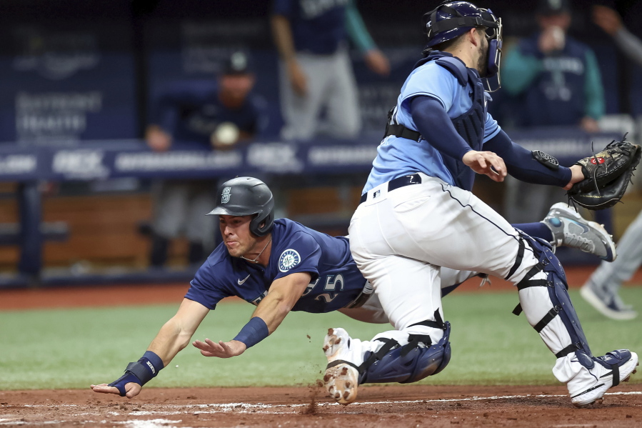 Seattle Mariners' Dylan Moore Dives to slides in behind Tampa Bay Rays catcher Mike Zunino to score during the fourth inning of a baseball game Tuesday, April 26, 2022, in St. Petersburg, Fla.